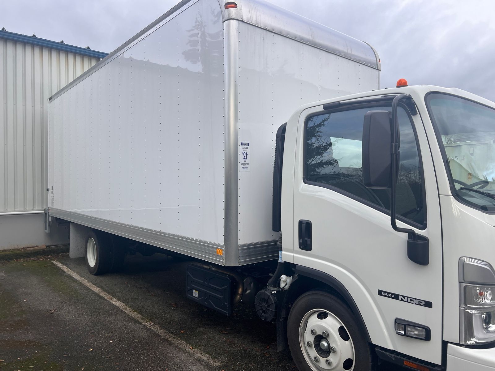 White box truck parked beside a building on a wet lot
