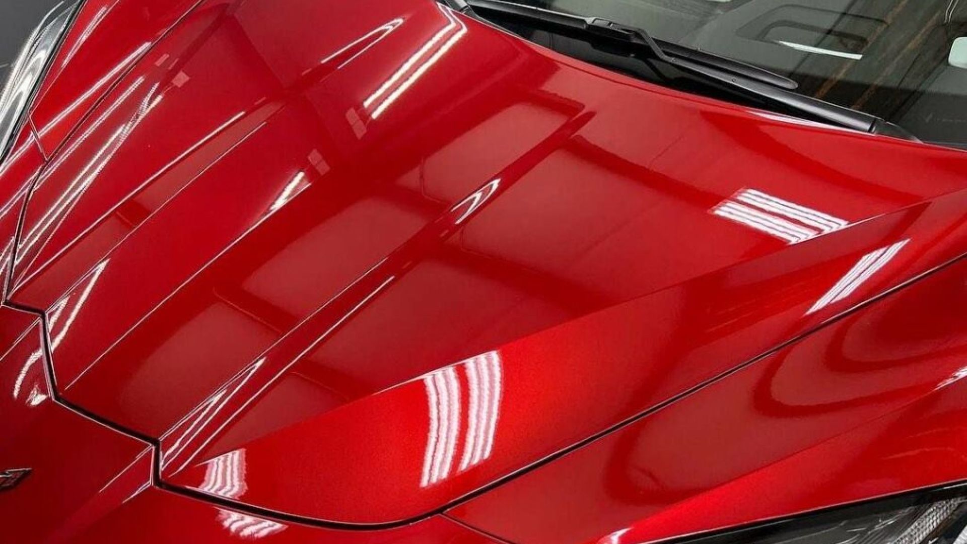 Close-up of a glossy red car hood with sharp reflections and black windshield trim