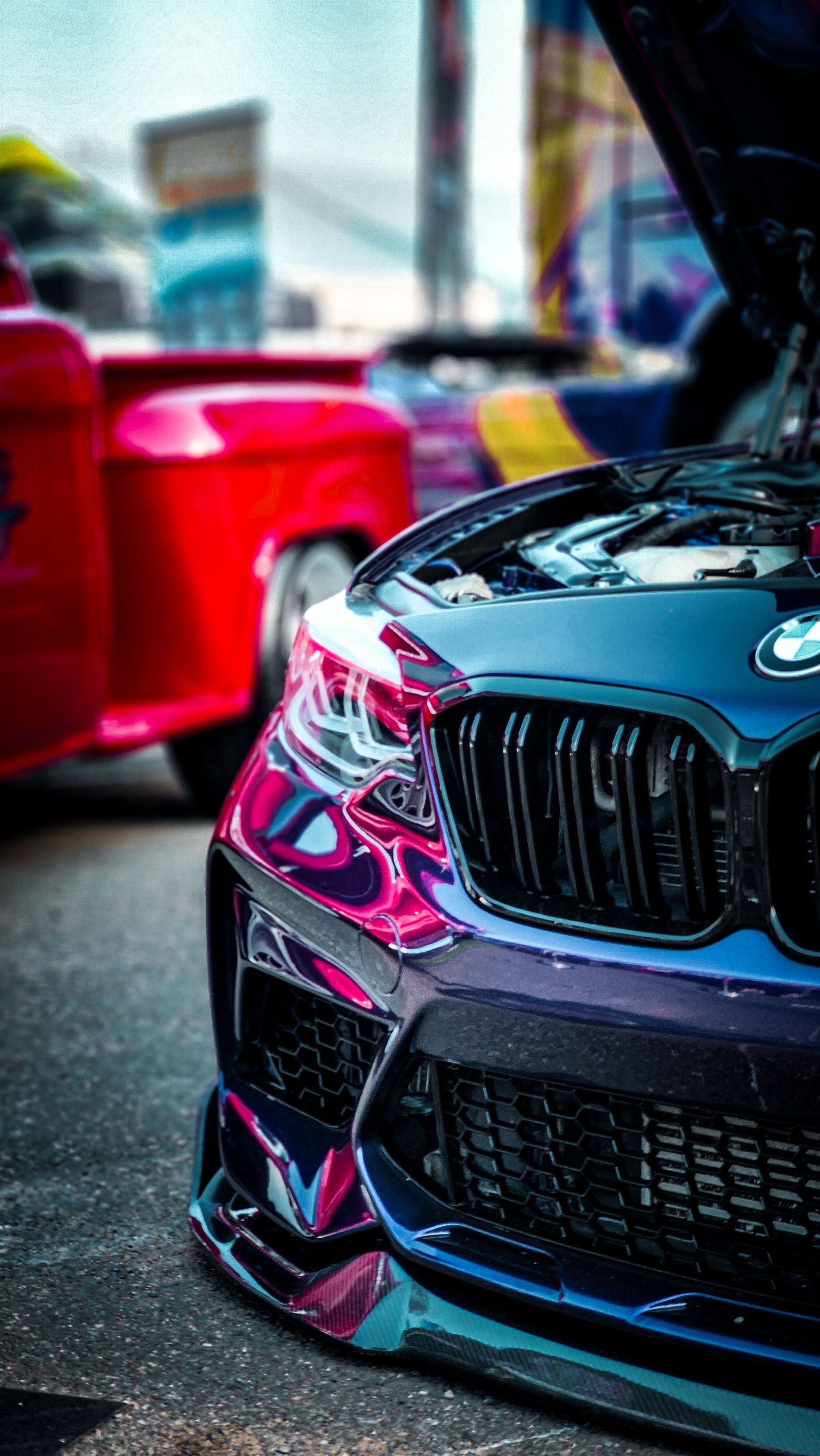 Glossy black sports car front end with pink reflections at a wet outdoor event