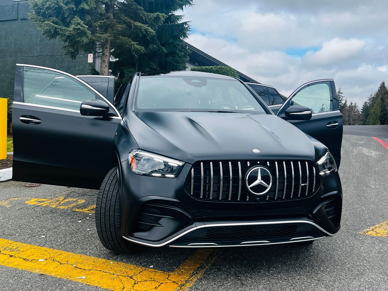 Black Mercedes SUV with open doors parked on a wet road in a cloudy setting