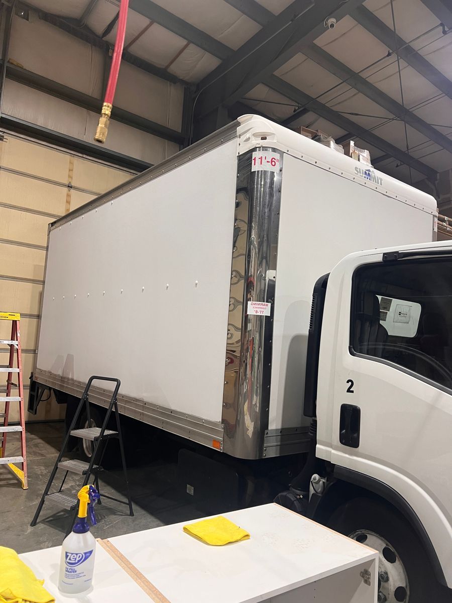 White box truck in a warehouse with its front cab visible and a ladder nearby