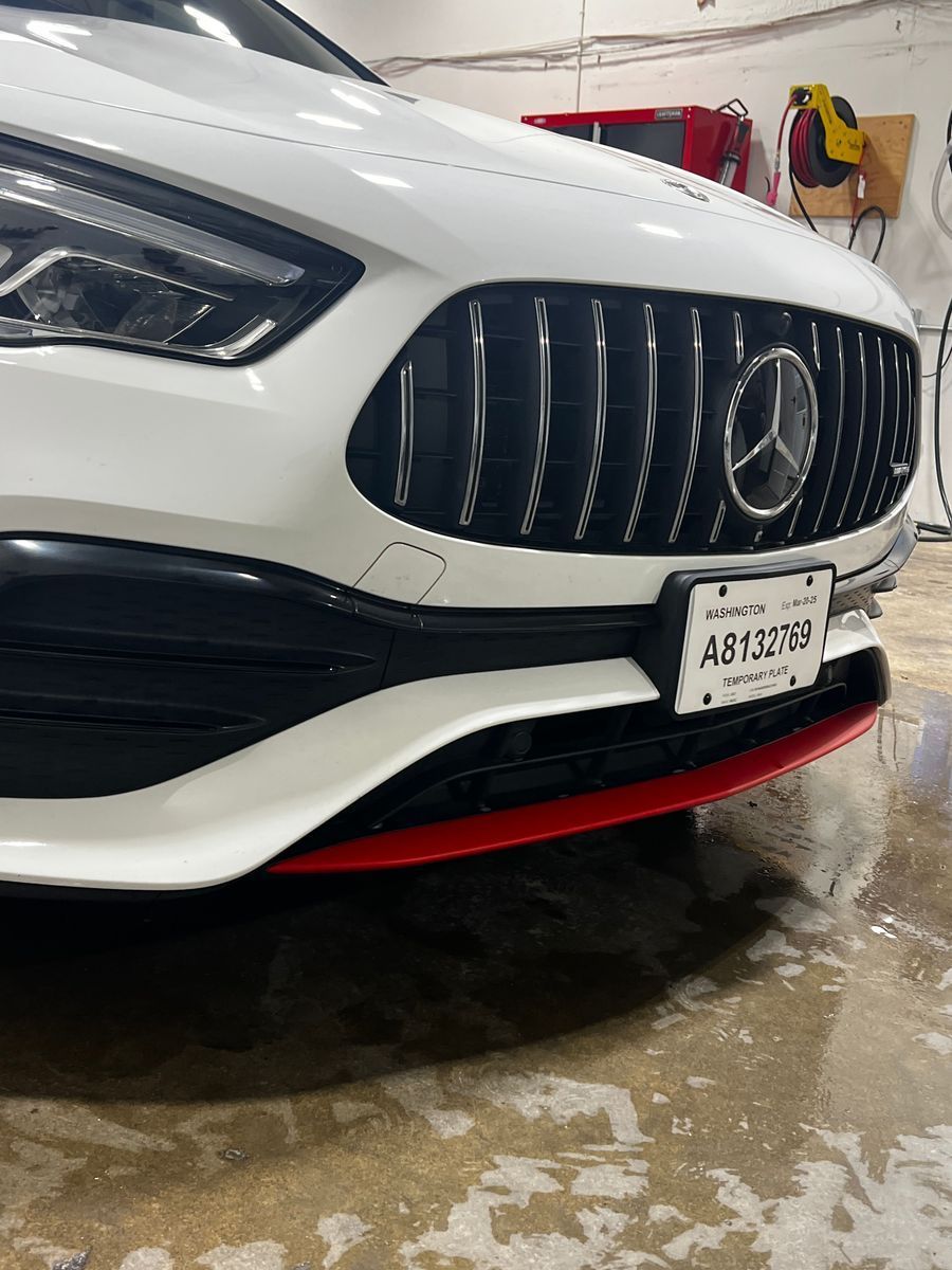 Close-up of a white Mercedes front grille with red trim in a wet garage
