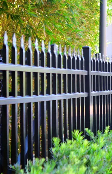 A close up of a black fence with trees in the background.