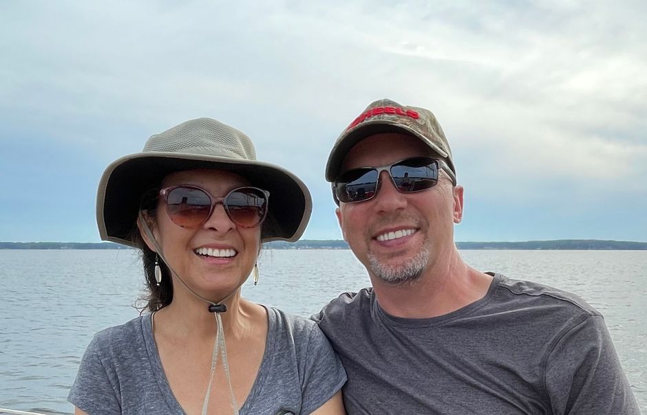 A man and a woman are posing for a picture in front of a body of water.