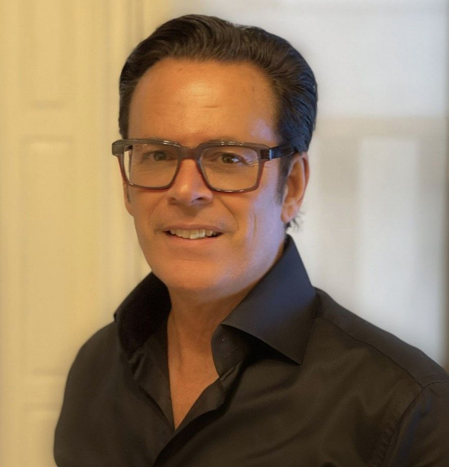 A man wearing glasses and a black shirt smiles for the camera