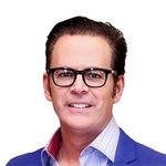 A man wearing glasses and a blue suit is smiling.