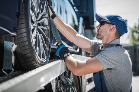Roadside assistance professional securing a disabled vehicle on a flatbed truck near Cameron