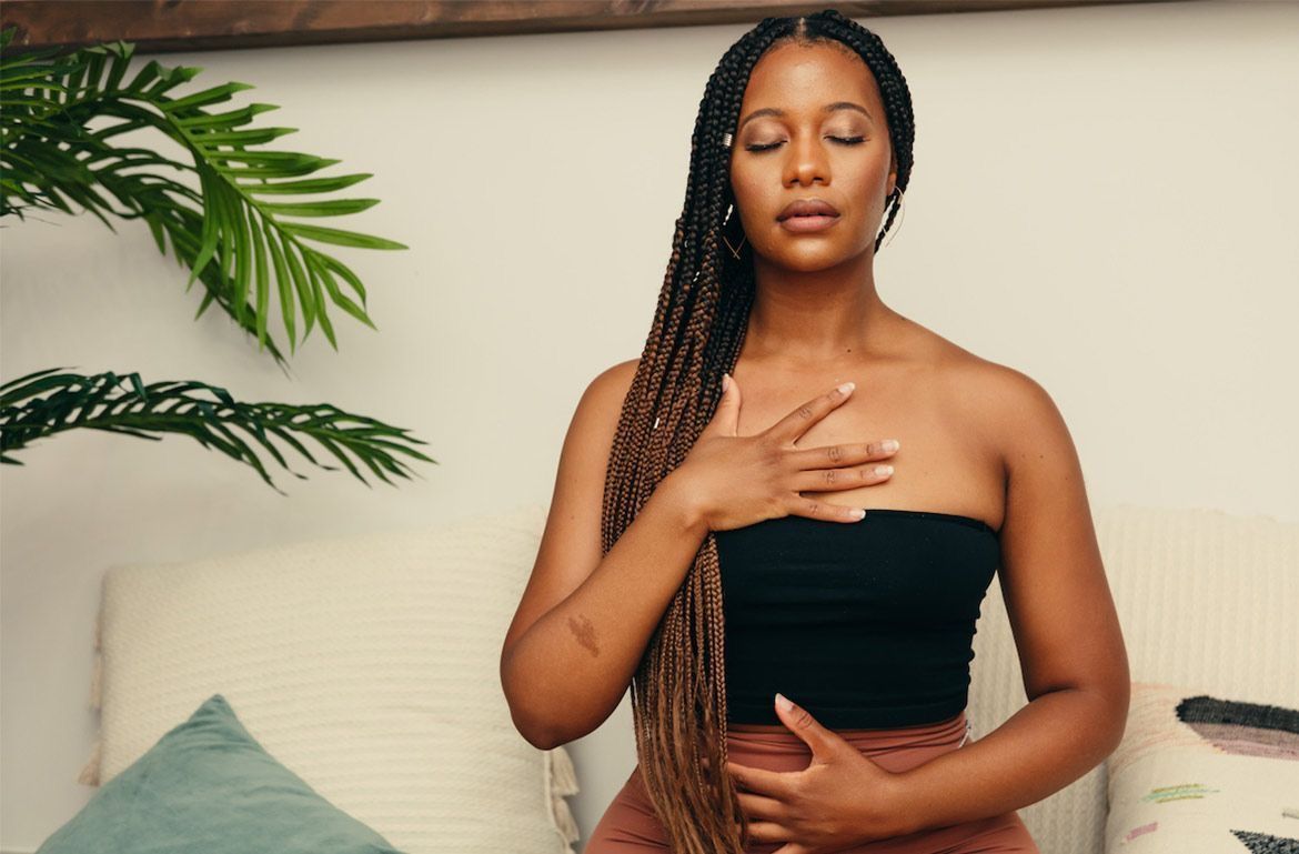 Mulher jovem com tranças, olhos fechados e mãos no peito e abdômen.