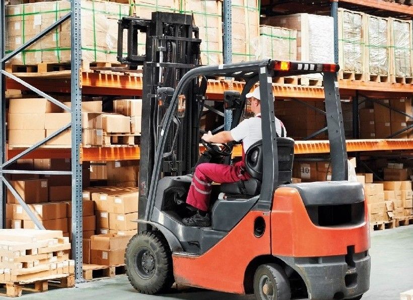 A Man is Driving a Forklift in a Warehouse Filled With Boxes — Advanced Industry Training In South Townsville, QLD