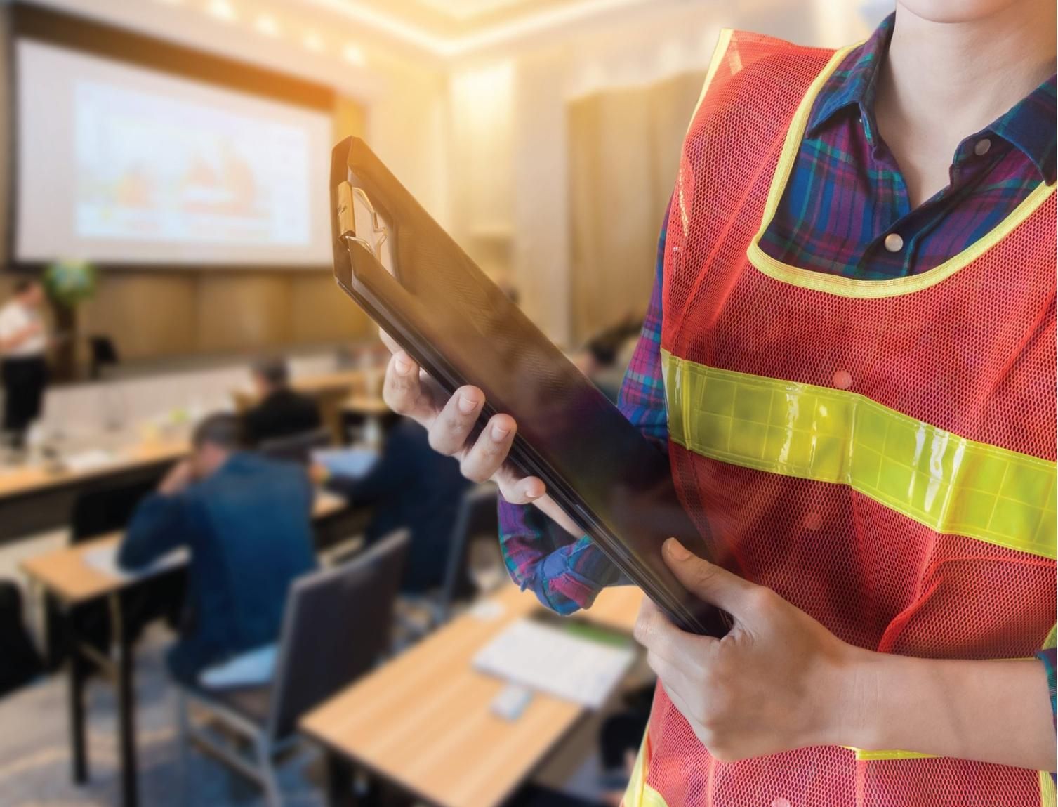 A Woman in a Safety Vest is Holding a Clipboard in a Conference Room — Advanced Industry Training In South Townsville, QLD