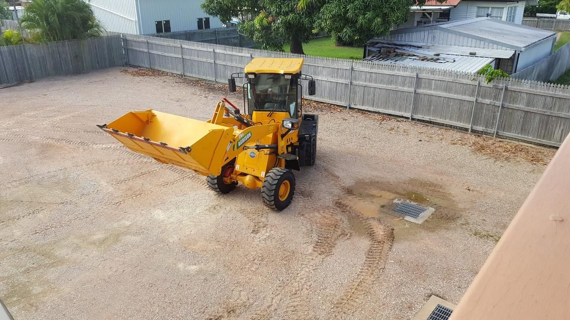 A Yellow Tractor is Parked in a Gravel Lot Next to a Fence — Advanced Industry Training In South Townsville, QLD