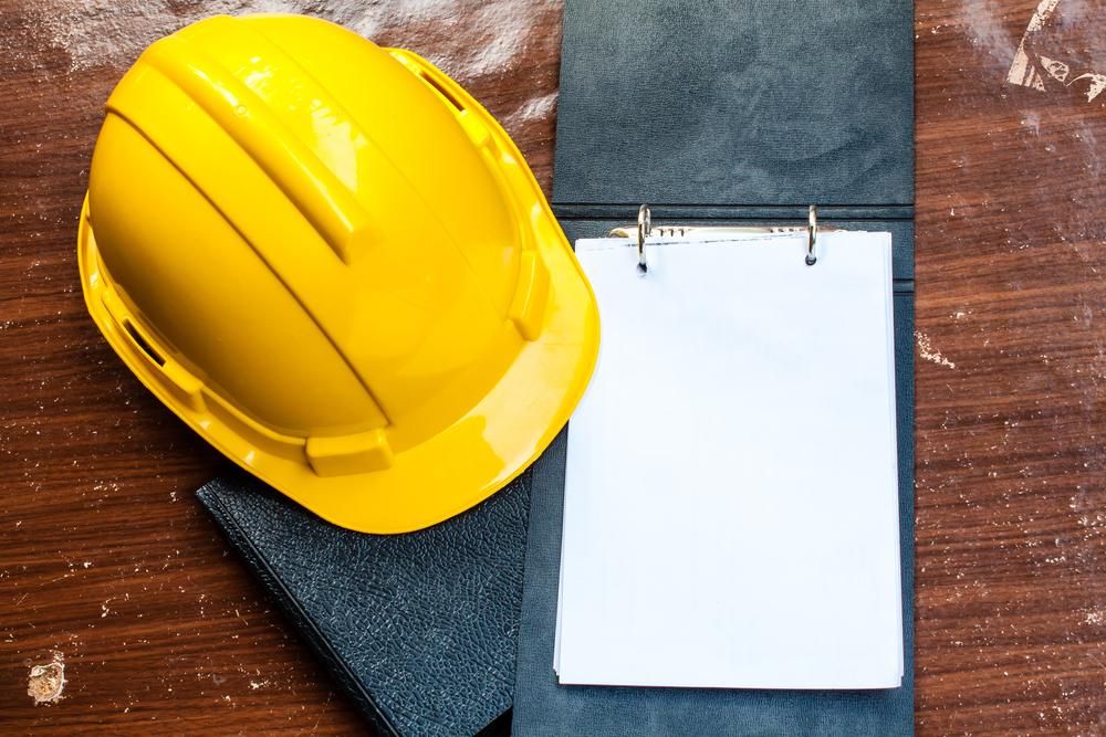 A Yellow Hard Hat is Sitting Next to a Notebook on a Wooden Table — Advanced Industry Training In South Townsville, QLD