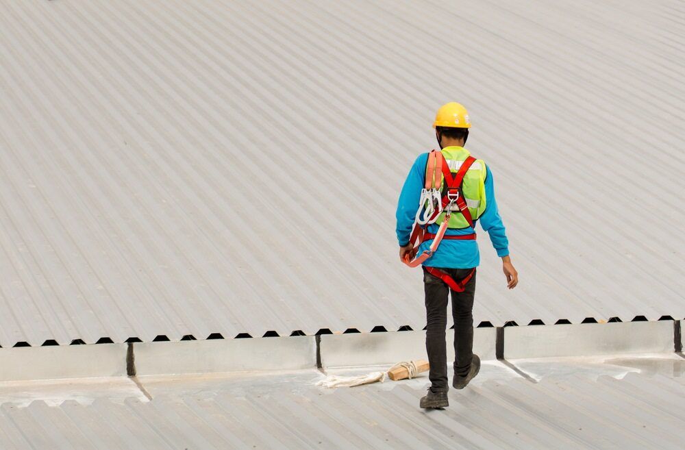 A Man Wearing a Hard Hat and Safety Harness is Walking on a Roof — Advanced Industry Training In South Townsville, QLD