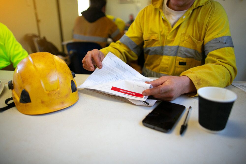 A Man in a Yellow Jacket is Sitting at a Table Holding a Piece of Paper — Advanced Industry Training In South Townsville, QLD