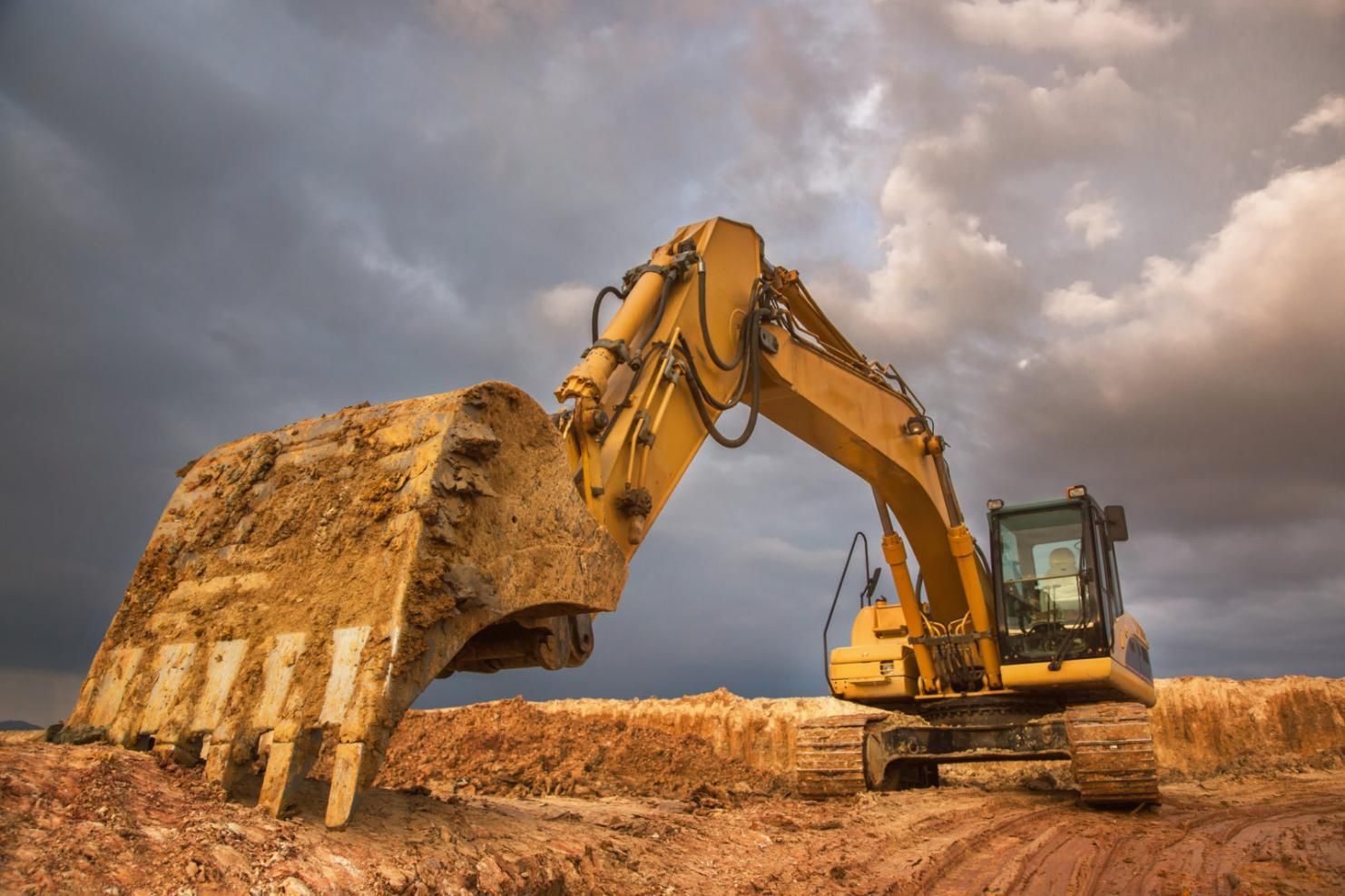 A Yellow Excavator is Digging a Hole in a Dirt Field — Advanced Industry Training In South Townsville, QLD