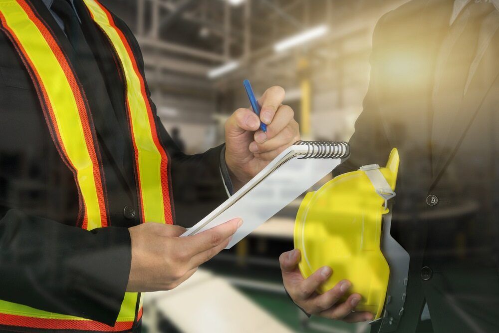 A Man is Writing on a Clipboard While Another Man Holds a Yellow Helmet — Advanced Industry Training In South Townsville, QLD