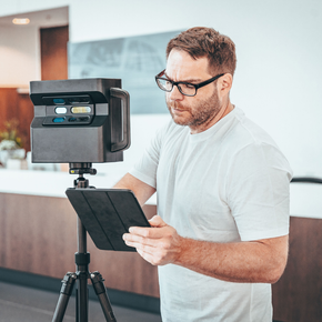 A man wearing glasses is using a tablet in front of a camera on a tripod