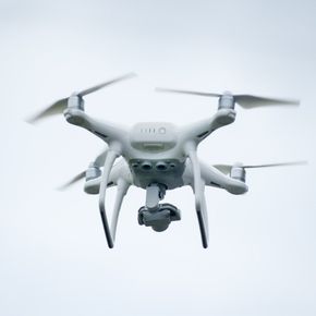 A white drone is flying through a cloudy sky