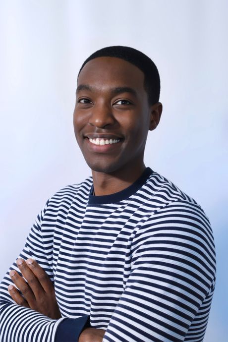 A man in a striped shirt is smiling with his arms crossed.