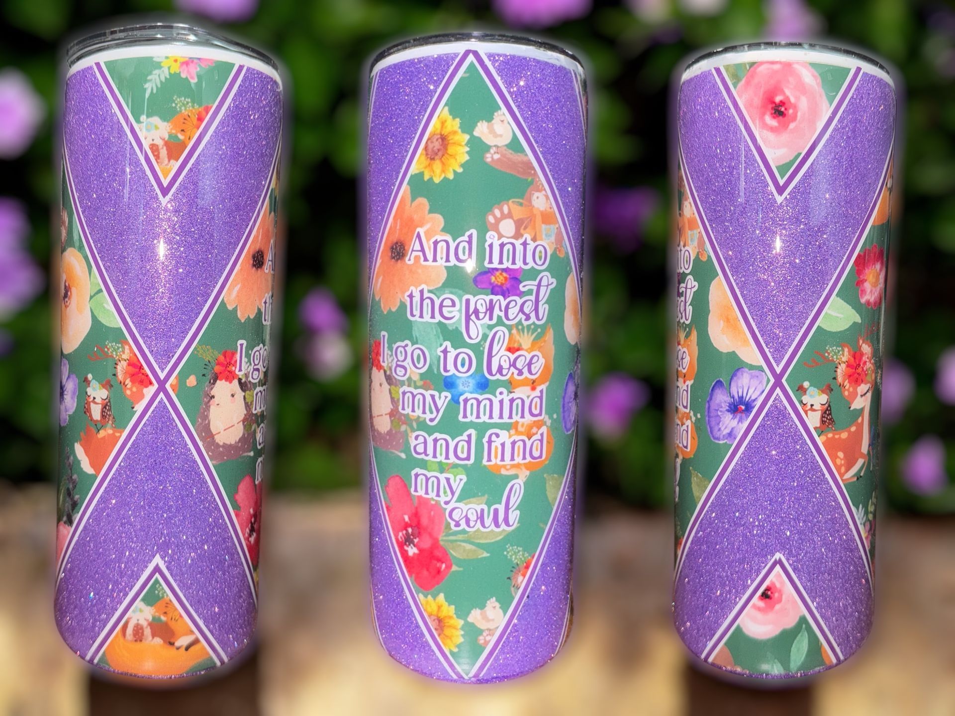 A floral design tumbler with a quote, sitting on a wooden surface with coffee beans scattered around.
