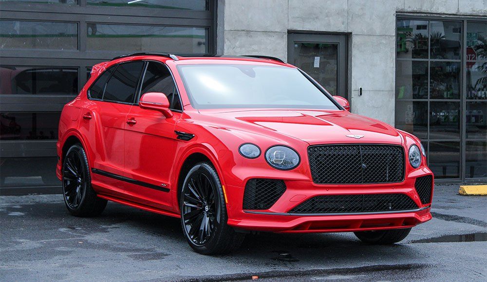 A red bentley bentayga is parked in front of a building.