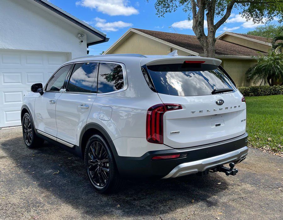 White Kia Telluride SUV parked on a driveway in front of a house on a sunny day.