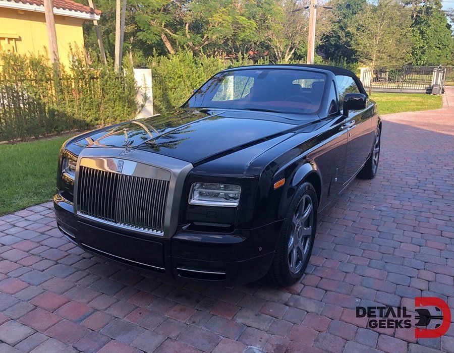 A black rolls royce convertible is parked on a brick driveway