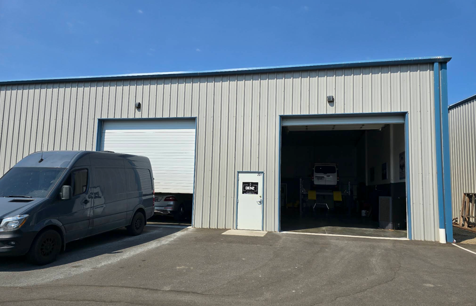 Industrial warehouse with a gray van parked outside and two open garage bays. | Benz Auto Clinic