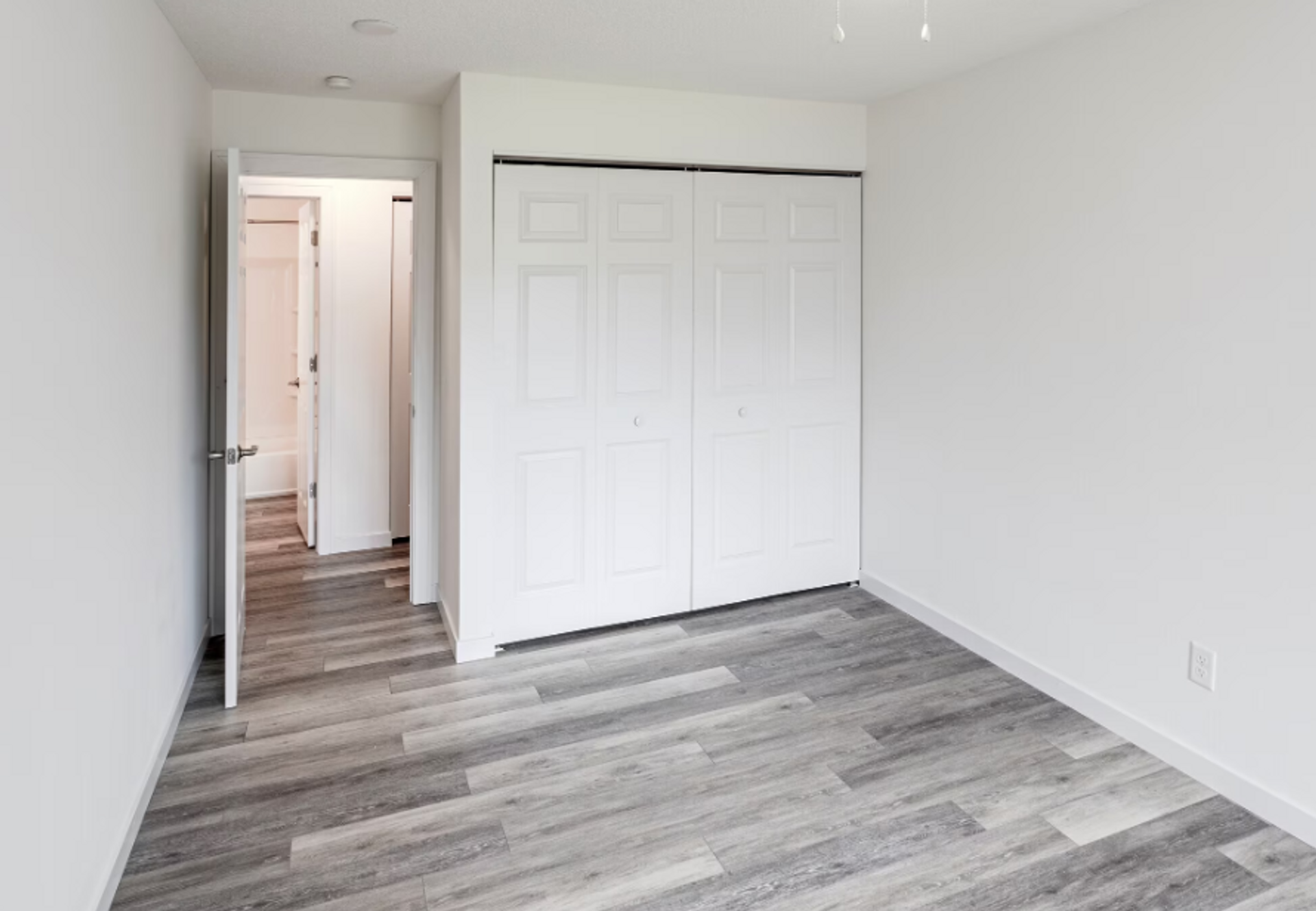 An empty bedroom with hardwood floors and white walls.
