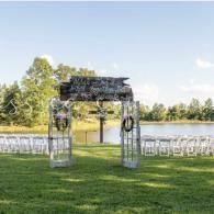Outdoor wedding arch by a lake with rows of white chairs on a grassy lawn