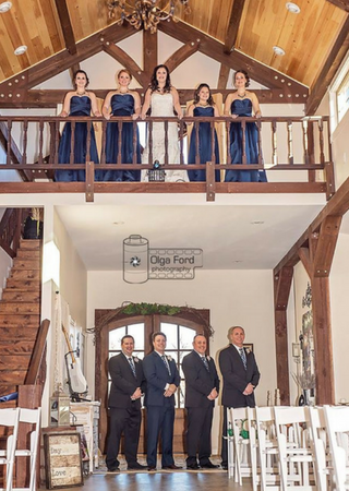 Women in blue dresses and men in suits pose in a wooden church interior under a balcony.