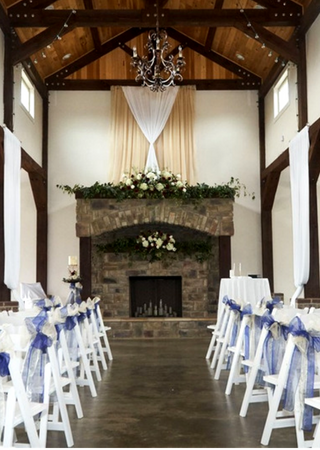 Decorated wedding ceremony aisle facing a stone fireplace and floral arrangement in a rustic hall
