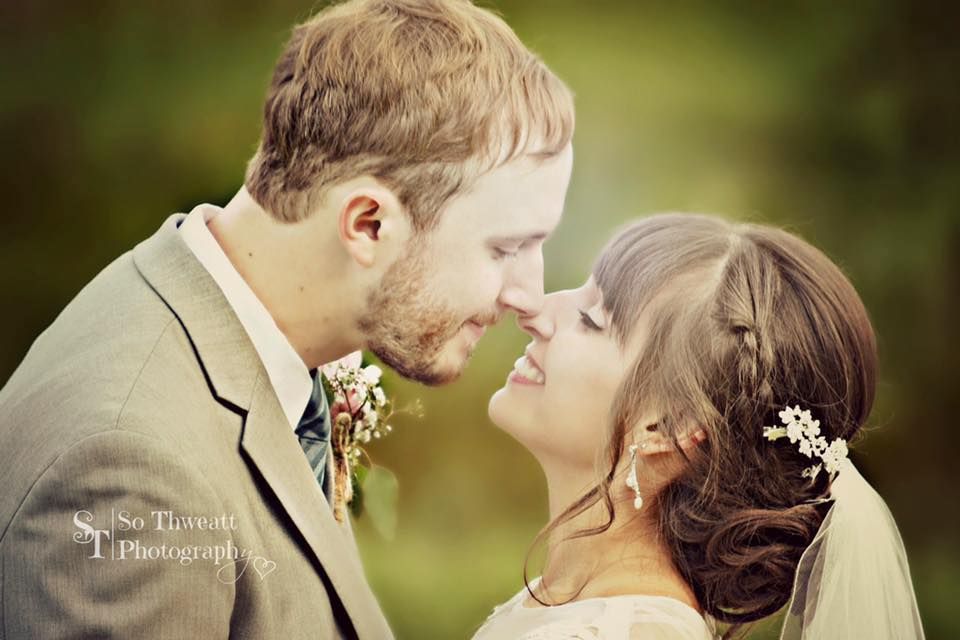 Couple in wedding attire leaning in for a kiss outdoors, with a soft green background.