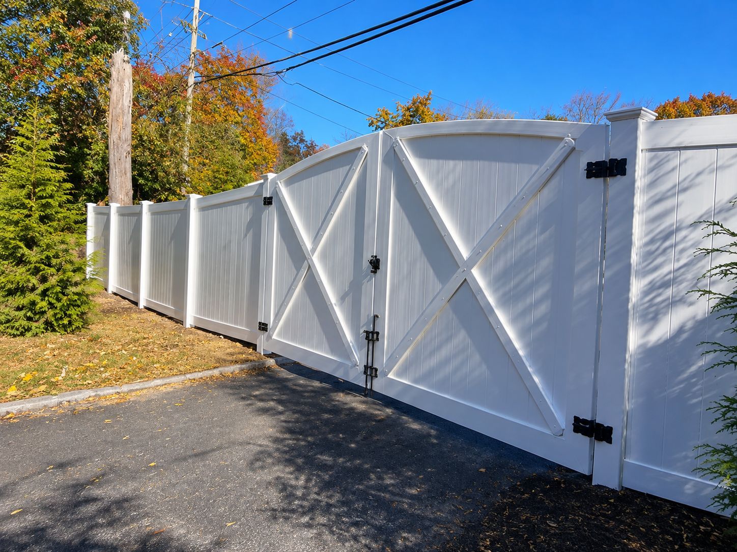 White wooden driveway gate and fence along a paved road on a sunny day