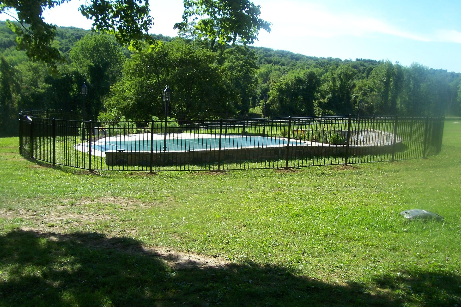 Round fenced pool in a grassy park with trees and hills in the background