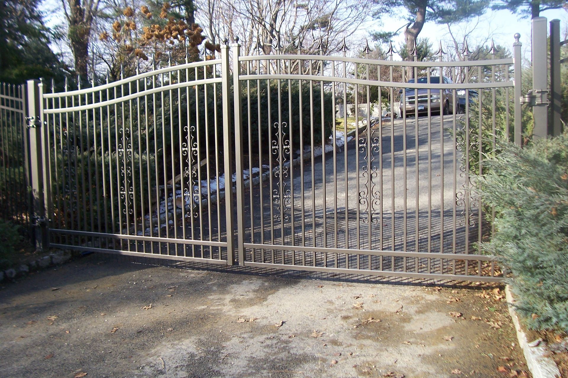 Closed metal driveway gate at the entrance to a residential property, with a paved driveway behind it.
