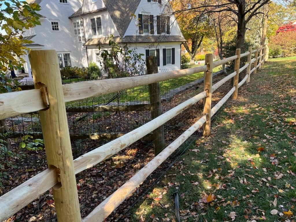 Wooden split-rail fence beside a white house in a leafy autumn yard