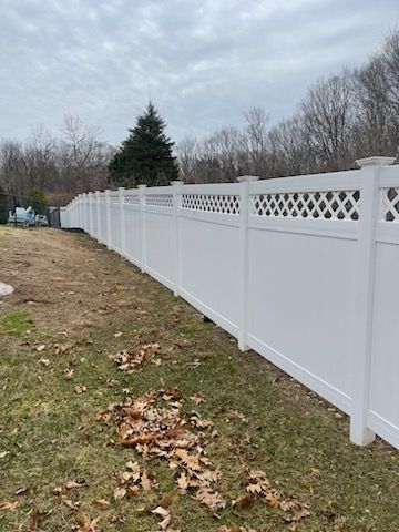 White vinyl fence along a grassy yard with fallen leaves under an overcast sky