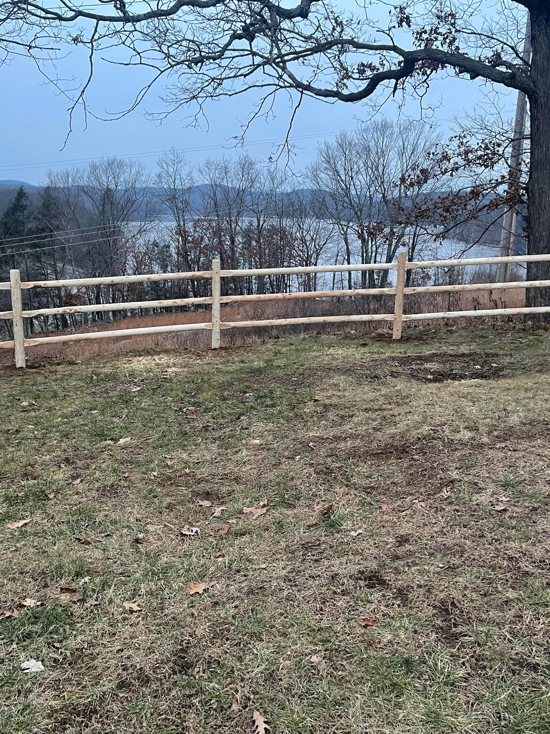 Wooden fence beside a grassy field with leafless trees under a cloudy sky