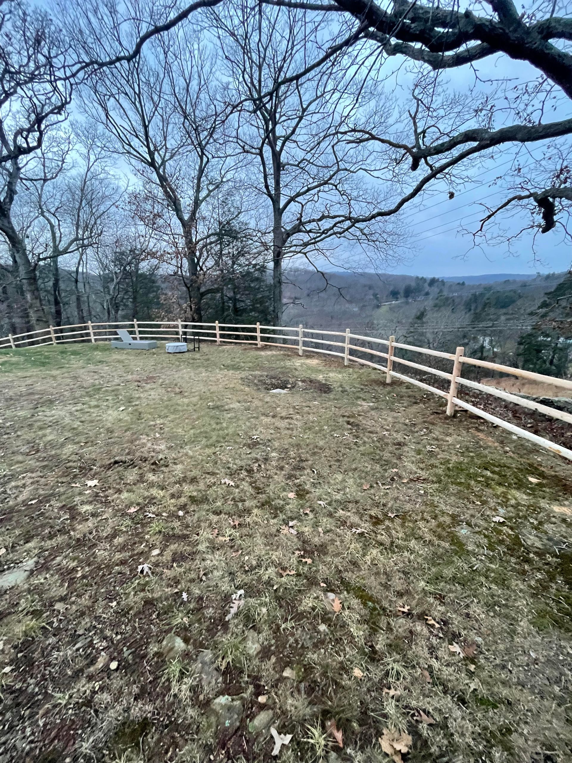 Leafless trees and a white fence around a grassy overlook with a distant valley view.