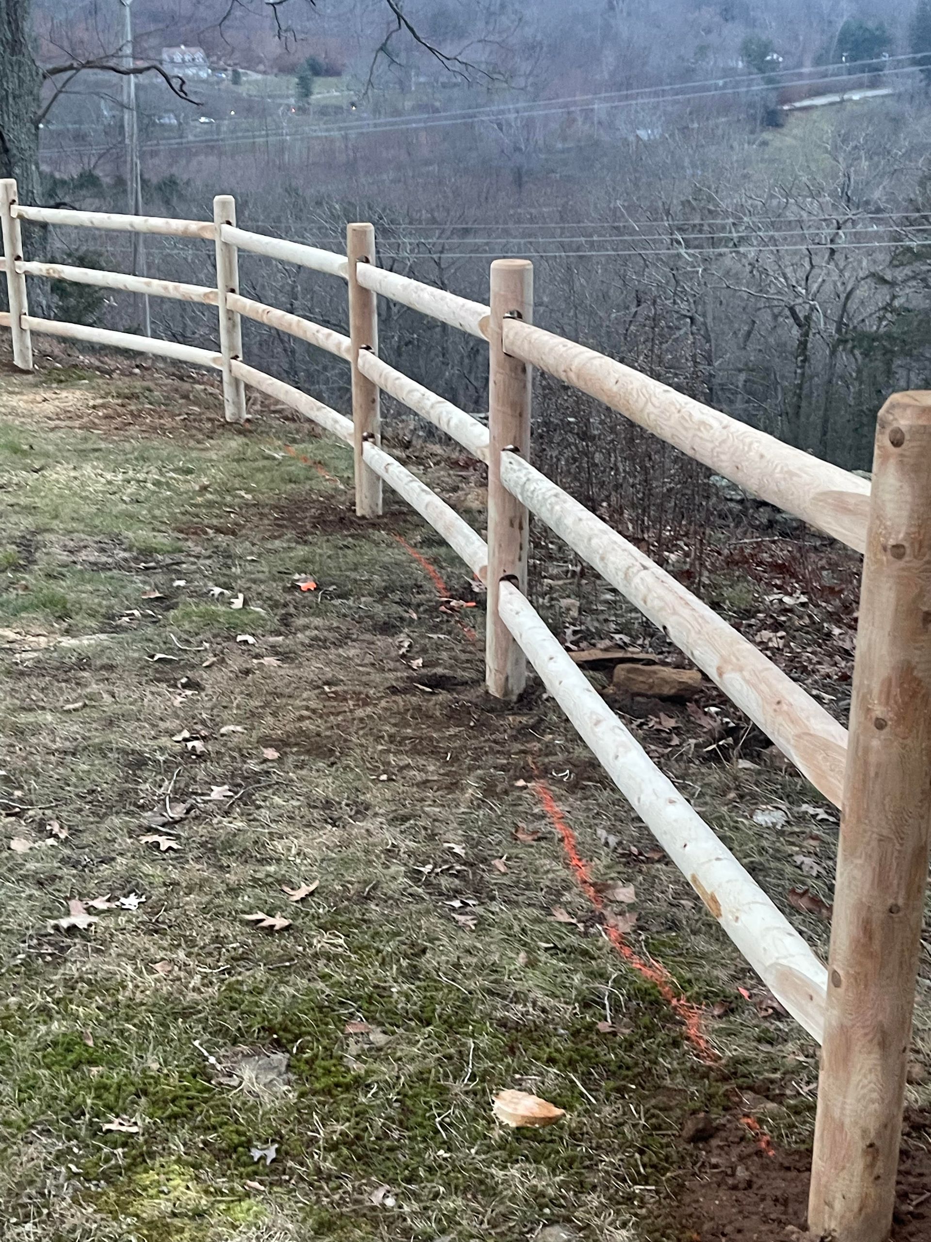 Wooden fence along a grassy hillside overlooking a wooded, misty valley