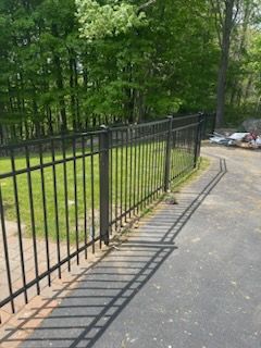 Black metal fence along a paved path beside green trees in a park-like area.