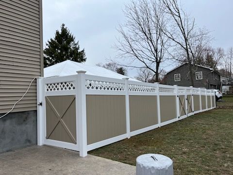 White vinyl fence enclosing a yard beside a house, with lattice top and gate on a grassy slope
