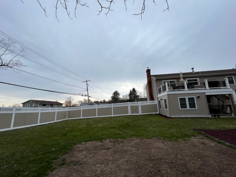 Backyard with white fence, grassy slope, and a two-story house under a cloudy sky