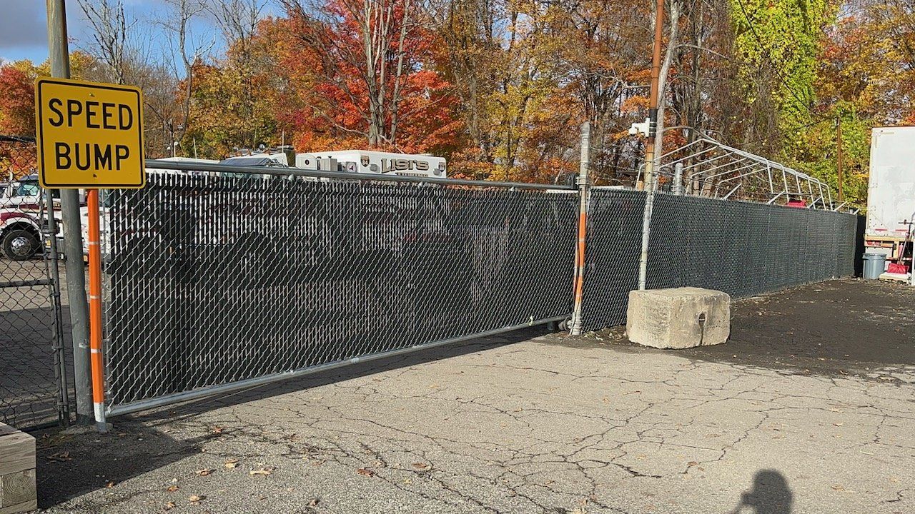 Speed bump sign beside a black mesh fence and orange posts, with autumn trees in the background.