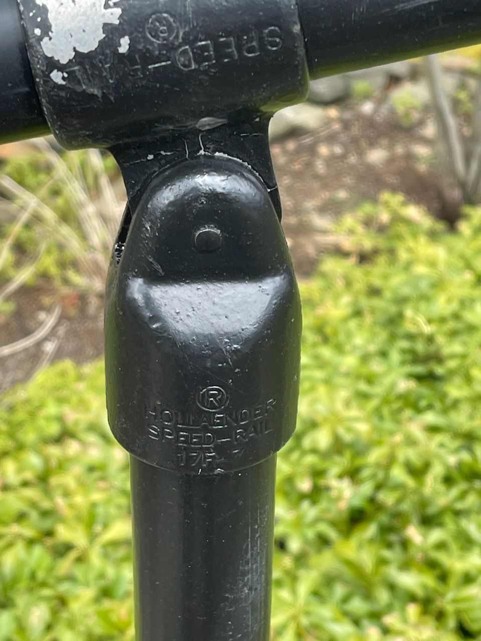 Close-up of a black metal pipe fitting outdoors with blurred green grass in the background