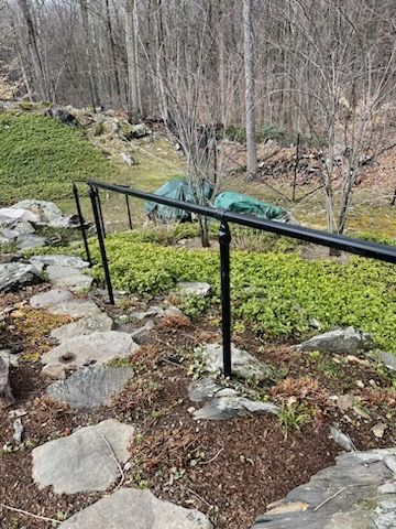 Stone steps with black metal railings beside a green hillside and bare trees