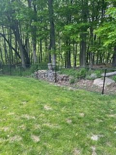 Grassy yard beside a wooded area with a black metal fence and stone border