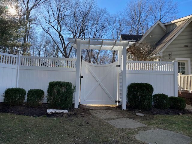 White backyard gate in a fenced yard with trimmed bushes and a house in the background