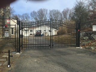 Black metal gate blocking a driveway in front of white buildings on a cloudy day